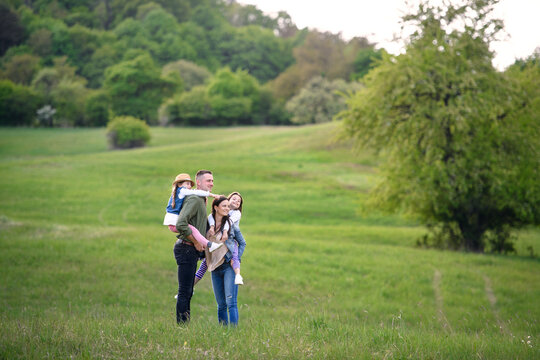 Happy family with two small daughters standing outdoors in spring nature.