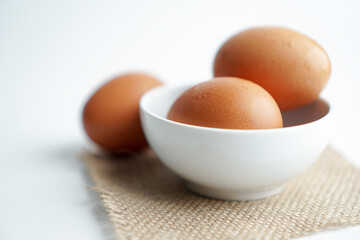 3 fresh poultry eggs on white bowl and brown fabric on white background.
