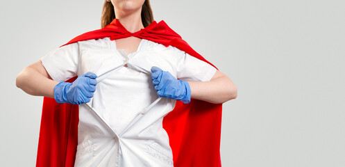 Close up portrait of a female doctor, wearing medical gloves and a red superhero Cape, tears her coat on her chest. Gray background. Copy space. The concept of the Power of a super hero for medicine © _KUBE_