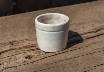 Old white ceramic salt shaker close - up against a wooden log