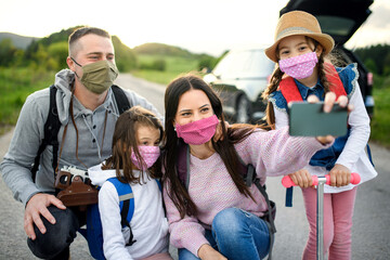 Family with two small daughters and face masks on trip outdoors in nature, taking selfie.