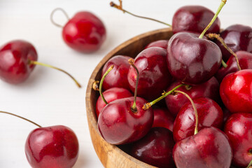 Top view of wooden bowl with cherries on white wooden table, with selective focus, horizontal