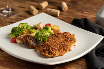 fish baked with crust and vegetables on white plate on a wooden table