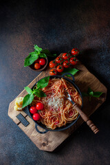 Spaghetti, pasta with tomato sauce and cherry tomatoes with basil on a dark background.