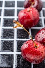 Aerial view of wet cherries on black and white tile, with selective focus, vertical