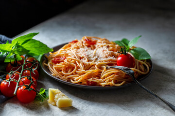 Pasta, spaghetti with tomato sauce, cherry tomatoes, fresh basil on a white concrete background.