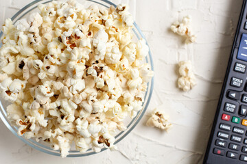 popcorn in a transparent glass bowl on white table with few popcorn beside bowl.