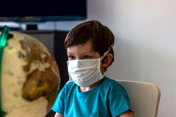 Fototapeta na wymiar Child with big globe, looking sad at the world during Covid 19 pandemic,virus that spread worldwide.Caucasian little boy wearing a face mask,the globe world map standing in front of him. Copy space.