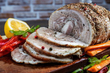 Traditional sliced baked pork garnished with herbs, lemon carrots and spices, prepared for serving on the festive table, close-up, shallow depth of field, selective focus. The concept of delicious