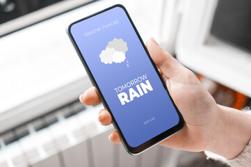 Woman check forecast weather on a smartphone at home in front of a window