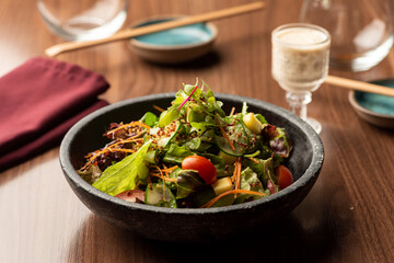 Green salad with lettuce arugula tomatoes on a ceramic bowl and dressing on cup