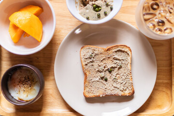 Chicken liver pate on bread with iced coffee, mango and soft boiled egg with seasoning sauce and ground pepper on wooden tray. Easy healthy breakfasts for your morning.