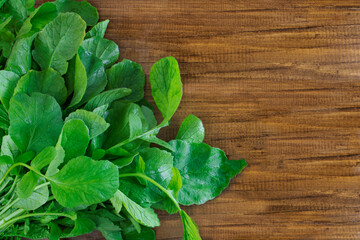 Young radish leaves on a wooden background. Useful leaves for salad. Greens for cooking. Great food. Copy space