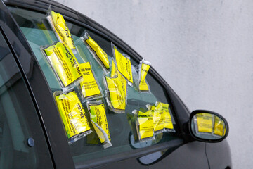 A car has numerous yellow parking tickets on the side window. It is parked in a restricted zone with residential parking only.