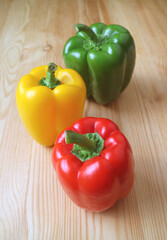 Vertical Image of Vibrant Tricolor Bell Peppers Isolated on Light Brown Wooden Background