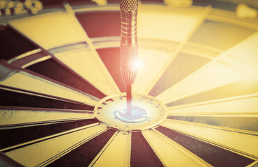Close up shot red darts arrow hitting on center of dartboard concept to target success in business on retro filter tone