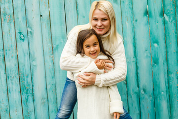 Small fashionable girl and her mother have fun together, keep hands together, pose against blue...