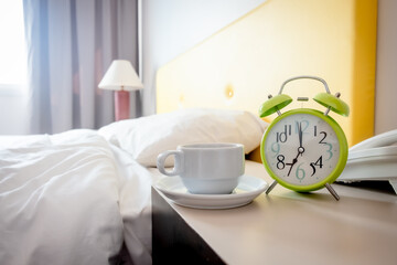 Ready-to-drink coffee cup Placed by the bed Add freshness before waking up to work. In a warm bedroom with a bright atmosphere And has an alarm clock showing the time.