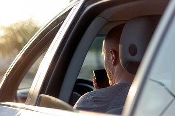 Cropped shot of young man using his phone while driving to destination.Shot of handsome man using mobile phone in the car.Close up image of man's hands holding and using modern smart phone.