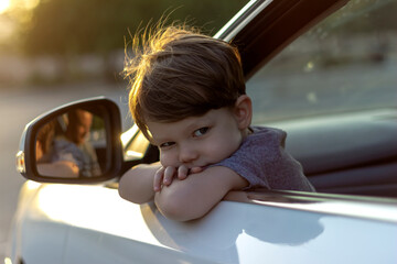 Boy looking out the window of the car,waiting to go on road trip.Cute little boy looking out of the car enjoying road trip with his father.Beautiful toddler leaning over the car door and looking away.