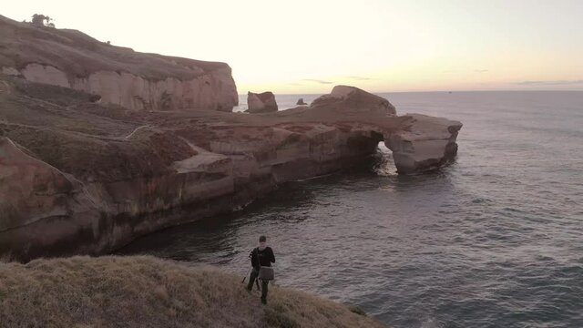 Man taking picture at the coastline at Tunnel beach, Dunedin, New Zealand during sunrise.