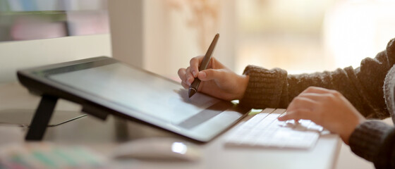 Female graphic designer working on drawing tablet with stylus pen on office desk