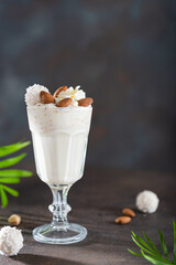 Milk Shake from almond, banana and coconut milk in a glass on dark background with palm leaves. Dairy free. Summer cocktail. Bar menu, recipe. Side view, copy space