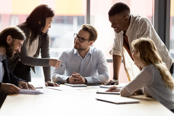 Multi-ethnic staff taking part at briefing group meeting, boss sitting at board room desk listens...