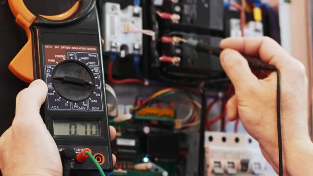 Electricians hands testing current  electric in control panel. Electrician engineer work  tester measuring  voltage and current of power electric line in electical cabinet control.