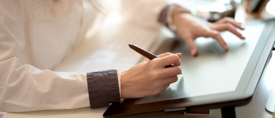 Female graphic designer working on drawing tablet with stylus pen on office desk