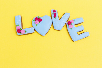 Inscription Love by homemade cookies with blue icing on yellow pastel color. Love romance concept. Valentines Day background. View from above.