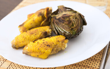 cooked fried chicken wings and halves artichokes on white plate