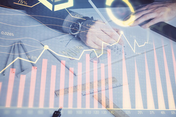 Double exposure of man's hands writing notes of stock market with forex chart.