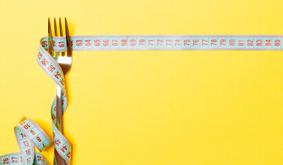 Diet and healthy eating concept with fork and measuring tape on yellow background. Top view of weightloss - obrazy, fototapety, plakaty
