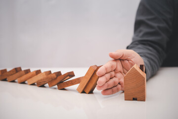 business man hand prevent falling wooden stick (dominoes) to the house model . risk management in...