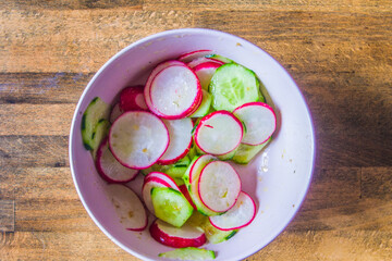 Bowl of radish and zucchini salad, with oil, salt and pepper on wooden board