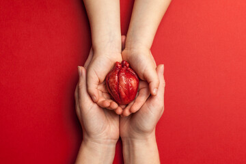 Human heart in mom and kid hands isolated on red background. Heart attack, failure.