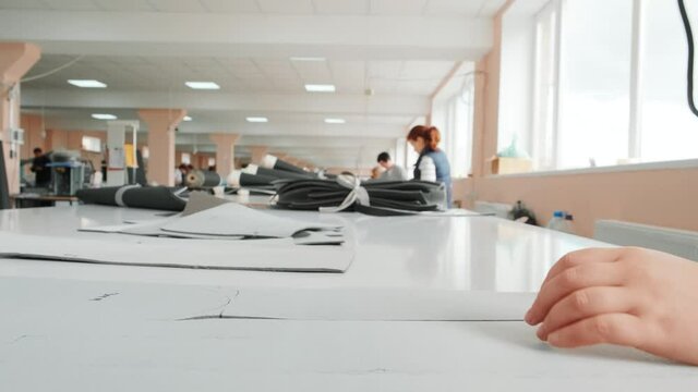 Female worker on a sewing manufacture uses electric cutting fabric machine. Sewing production line