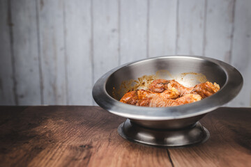 Close-up of a bowl full of marinated FRESH RAW ORGANIC CHICKEN DRUMSTICK with lots of spices on a dark brown wooden table.