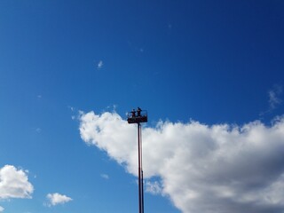 people at the top of a cherry picker or tower and blue sky with cloud