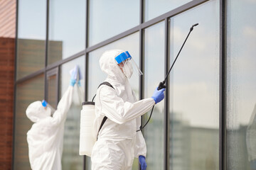 Portrait of two workers wearing protective suits spraying chemicals over building outdoors during...