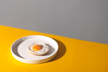 Fried egg on a round plate on a yellow table with hard shadows. The concept of creativity and minimalism in cooking. Copy space.