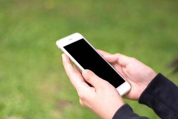 Close up female hands holding smart phone black screen for copy space with grass field blurred background.