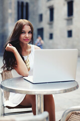 Young gorgeous woman drinking coffee while sitting with open laptop computer outdoors