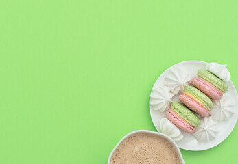 The cup of cappuccino and delicious macarons with white merengues on white plate  on green background. Happy day, breakfast, good morning concepts. Greeting card. Flat lay style with copy space.