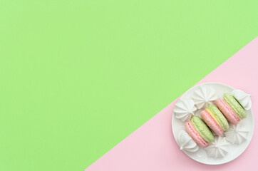 Delicious macarons with white merengues on white plate on double green and pink  background. Happy day, breakfast, good morning concepts. Greeting or invitation card. Flat lay style with copy space.
