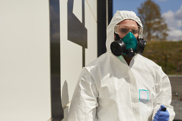 Waist up portrait of male worker wearing hazmat suit standing outdoors by building in sunlight during disinfection or cleaning, copy space