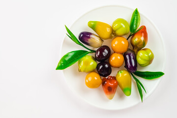Top view of colorful traditional Thai dessert called Deletable Imitation Fruits (Kanom Look Choup) decorate with green tea leaves on white plate isolated on white background