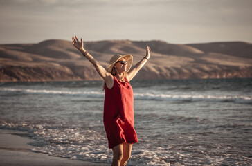 Woman in red with arms outstretched by the sea at sunrise enjoying freedom and outdoors life