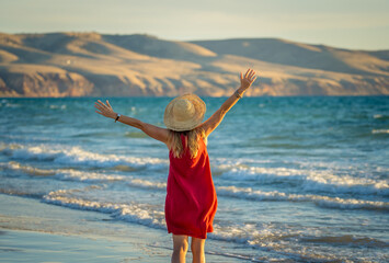 Woman in red with arms outstretched by the sea at sunrise enjoying freedom and outdoors life